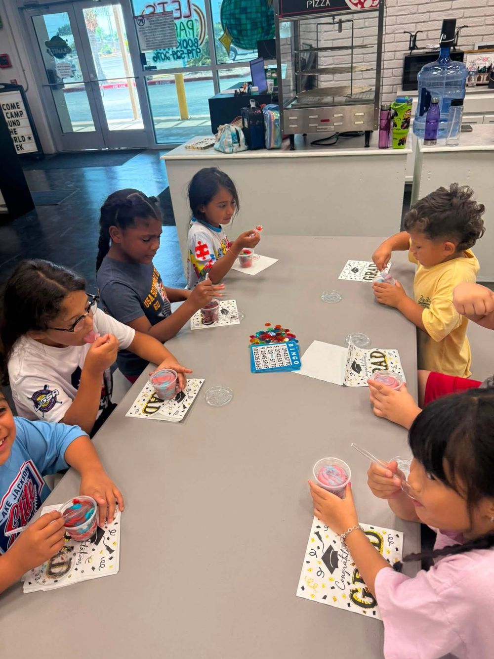 Children seated around a table at a daycare eating cups of water ice